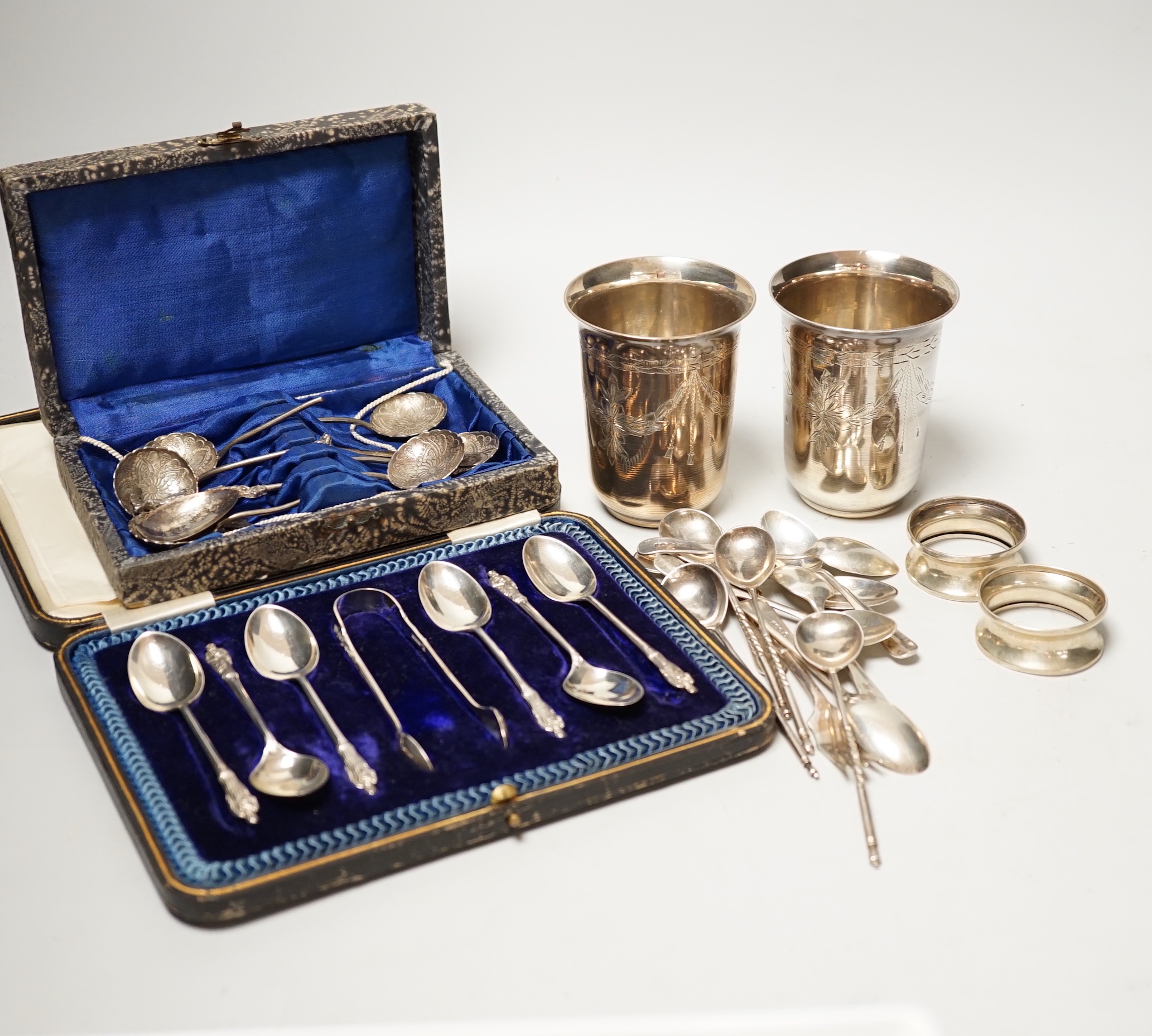 A pair of engraved white metal tumblers, stamped 'K980', four Russian 84 zolotnik spoon, a cased set of silver silver teaspoons with tongs, two silver napkin rings and other minor silver and white metal flatware.